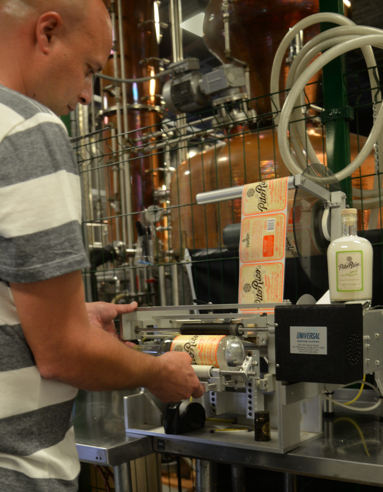 Cesar Torres, the main distiller and blender (official title: Jack of Spades and Trades) at Sol Taino Spirits, positions a rum bottle on a labeling machine. Sol Taino Spirits is the only certified craft distillery in Puerto Rico. Photo by Sarah Price
